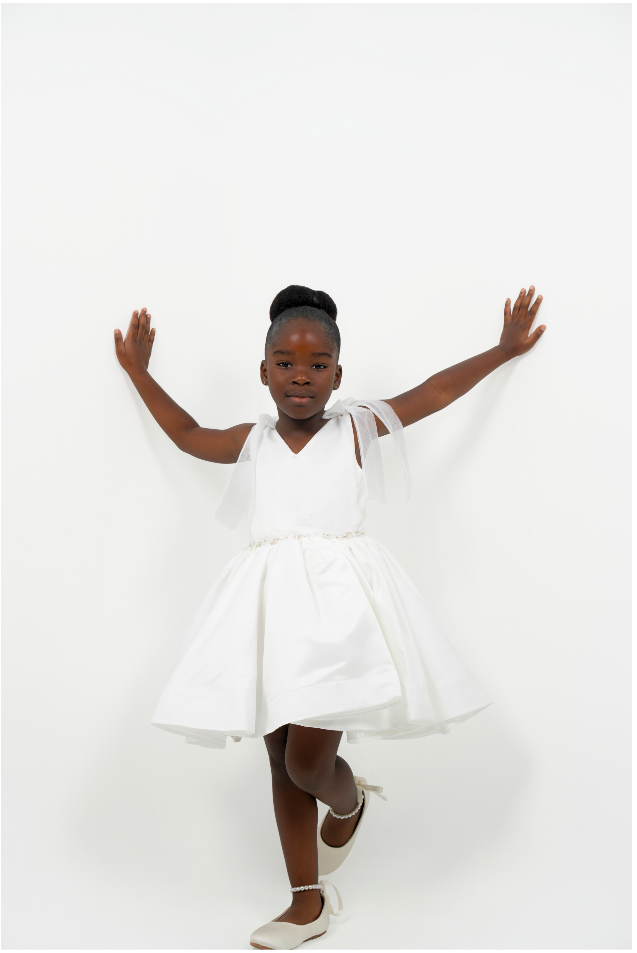 Girl wearing white satin dress with bow straps and full skirt, perfect for flower girl or birthday